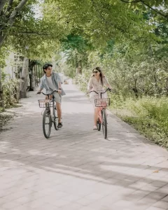 Man and woman riding bicycles on a quiet paved path surrounded by greenery.